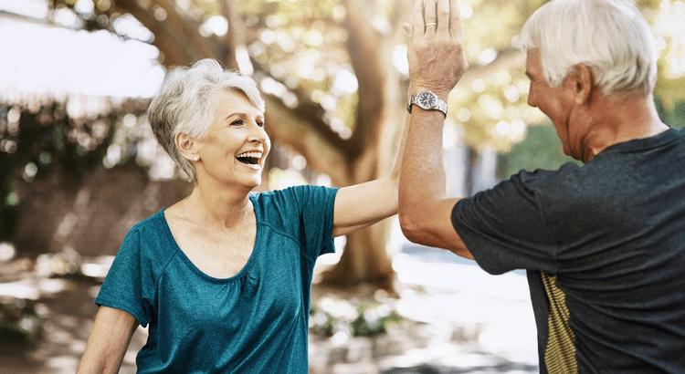 Two senior individuals happily giving each other a high five outdoors, enjoying an active lifestyle.